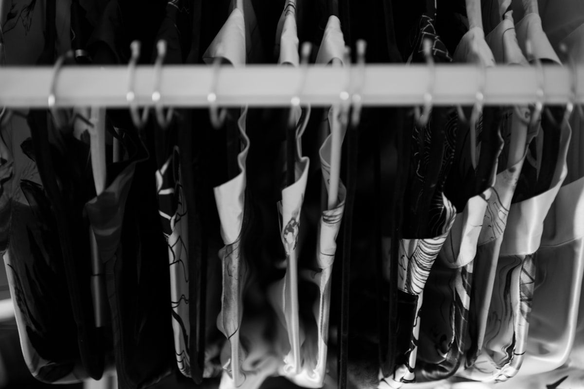 A neatly organized custom closet interior with double hanging rods, drawers with dividers, angled shoe shelves, pull-out accessory racks, a hidden hamper, and a small bench beneath bright overhead lighting.