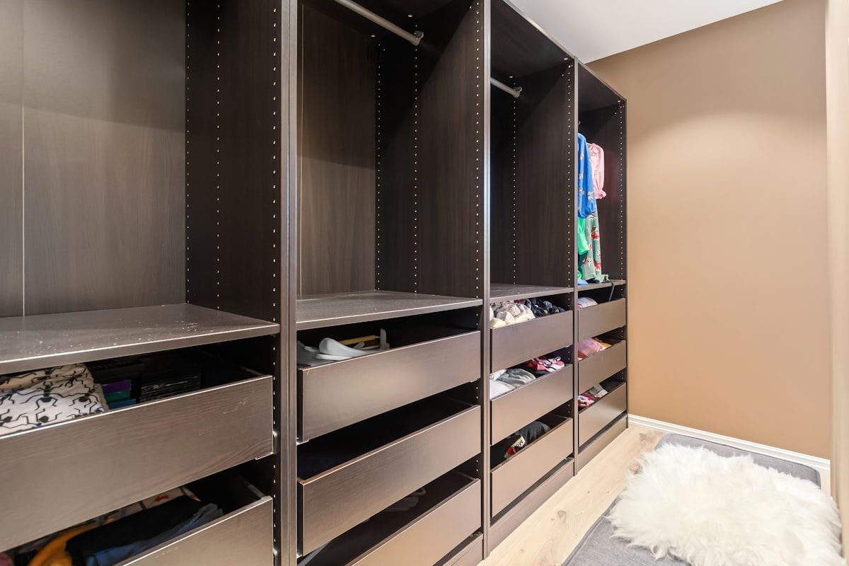 A close-up view of a custom closet interior with smooth light-colored panels, soft-close drawers partly open, sturdy metal hanging rods, neatly finished cabinet edges, and neatly aligned shelves showing durable built-in construction.