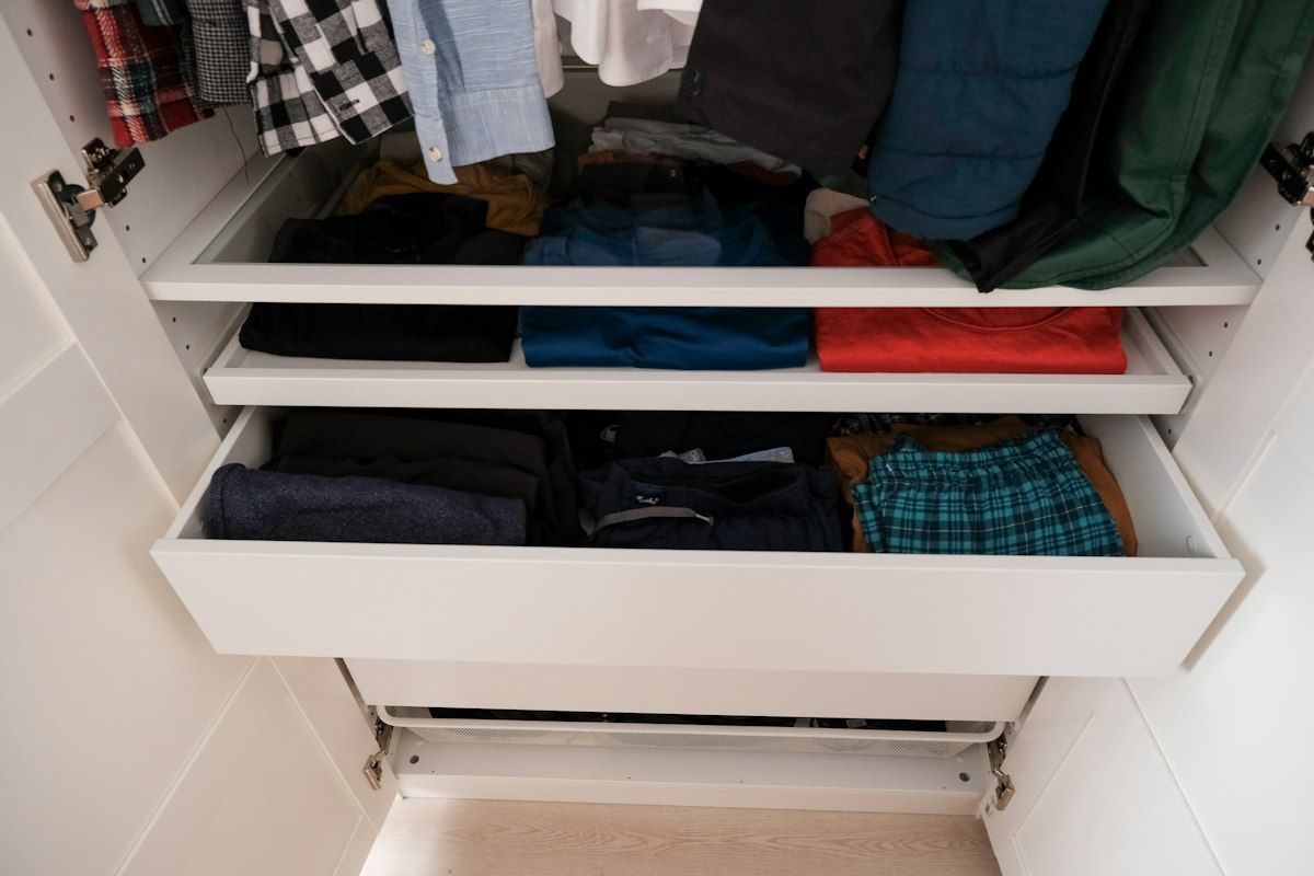 A bedroom closet emptied onto the floor with shirts, pants, shoes, and bags sorted into separate piles, plus four open bins placed beside the closet for keep, store elsewhere, donate, and toss.