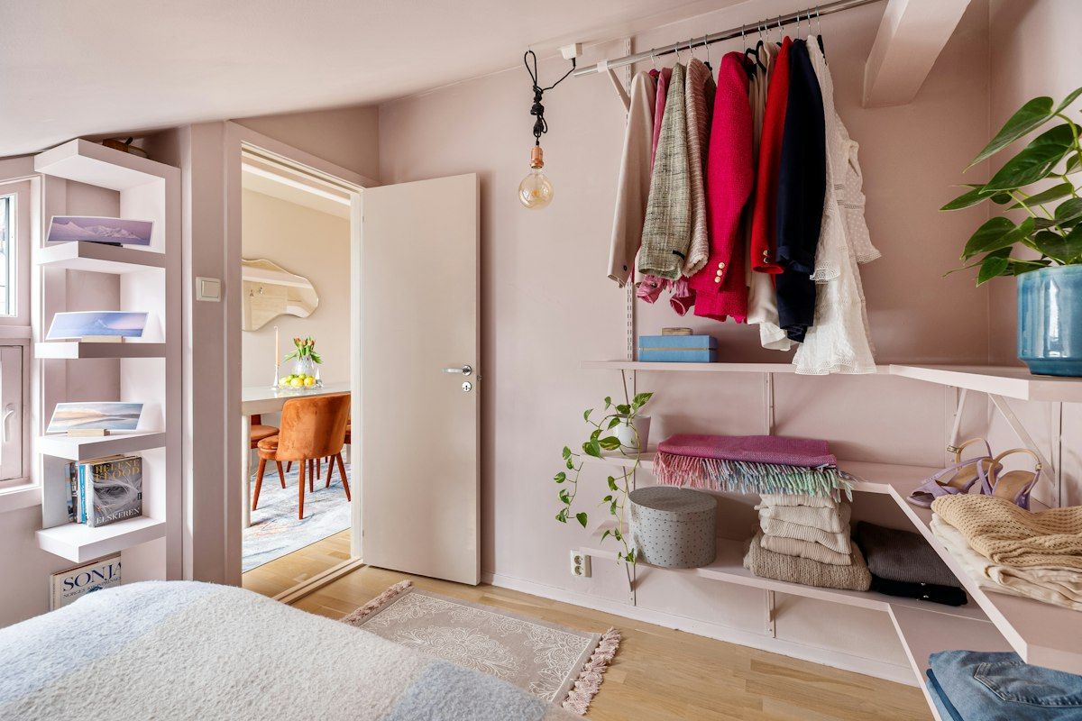 A bright bedroom closet split into two halves: one side has a simple white modular DIY organizer with open shelves and hanging rods, while the other side has a seamless custom built-in with fitted cabinets, drawers, and trim that reaches the walls and ceiling.