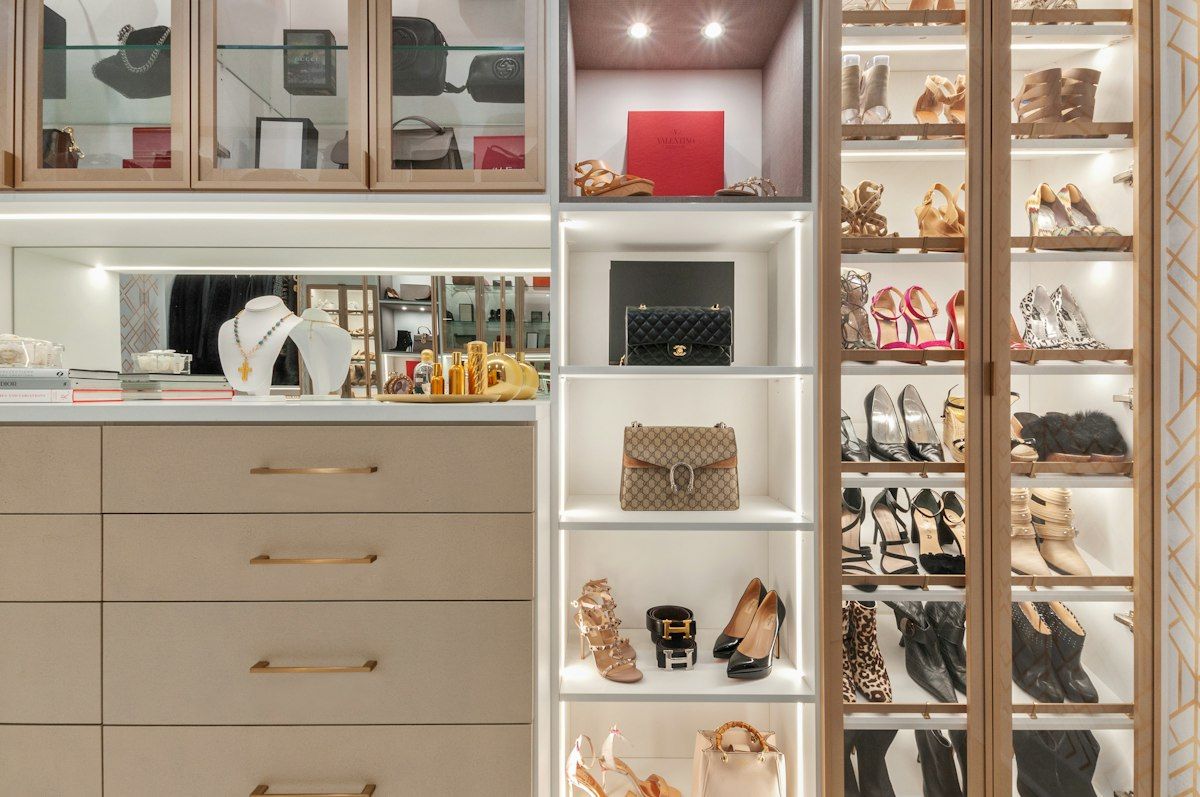 A tall custom closet wall filled with floor-to-ceiling adjustable shoe shelves, with neat rows of different footwear at varying shelf heights: flat sandals on lower shelves, sneakers in the middle, and taller boots on upper shelves, all in a bright built-in closet with unused vertical space minimized.